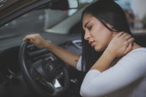 Beautiful woman rubbing her neck, feeling sore after long drive. Female driver having neck pain after whiplash injury in car crash. Woman suffering from back pain. Healthcare, safety, pain concept